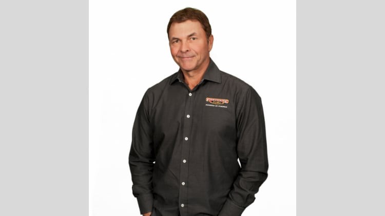 A headshot-style portrait of a man with brown hair in a dark Firehouse Subs-branded button-down shirt, smiling, against a plain white background.